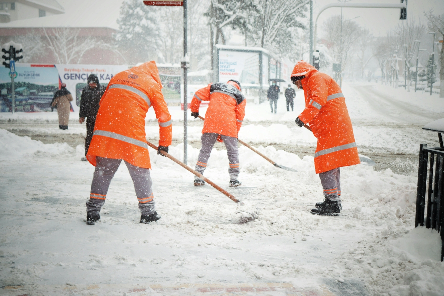 UHP Unterhaltsreinigung - Sauberkeit und Service mit Verantwortung - Mehrere Arbeiter in orangefarbenen Warnwesten und Mützen räumen im Winter mit Schaufeln eine schneebedeckte Straße oder einen Gehweg frei.